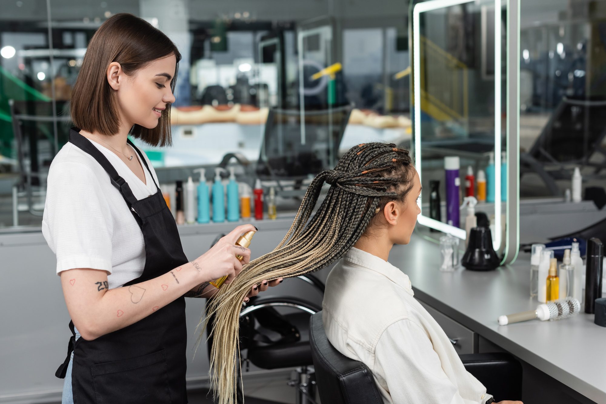 Hair Salon Tattooed Beauty Worker In Apron Applying Hair Product On Braids Of Woman In Salon Spray.jpg